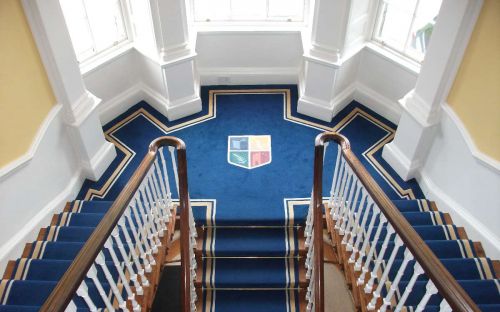 Hand tufted stair carpet with college crest on landing